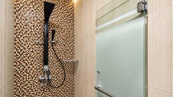 A modern shower area with a mosaic tile wall, a glass door, and a metal handrail.