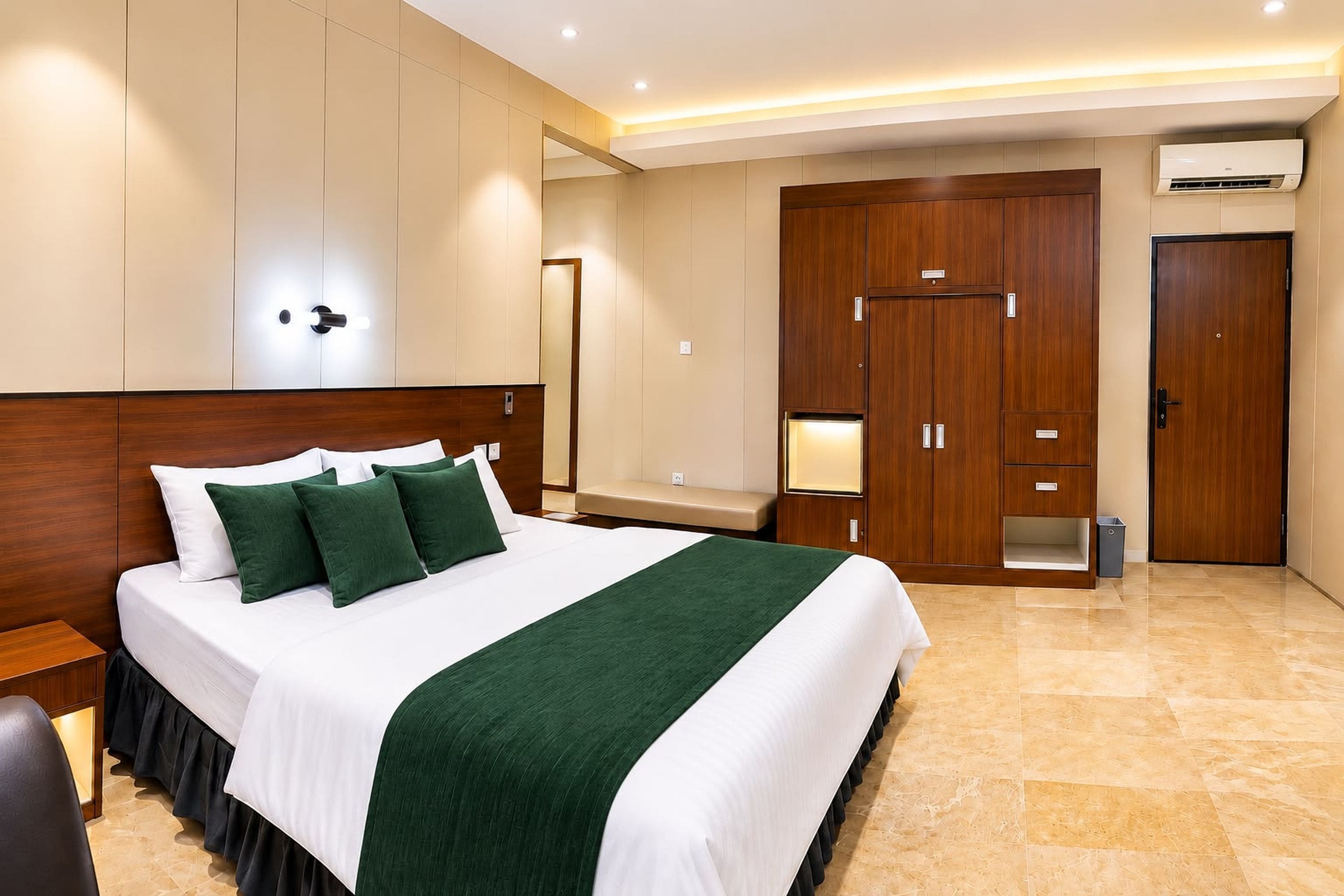 Een hotelkamer met een groot bed, een houten garderobe, een bankje en een airconditioning.