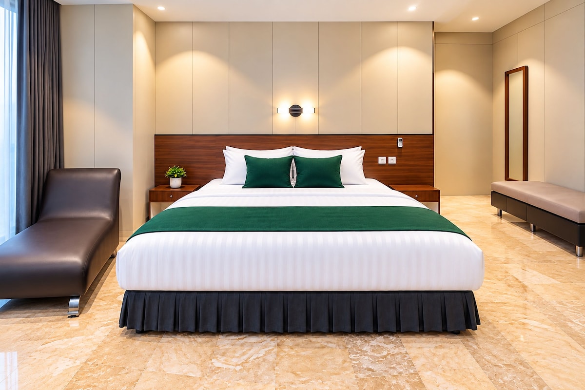 A modern hotel room with a large bed, a wooden headboard, a bedside table with a plant, a bench, and a large mirror.