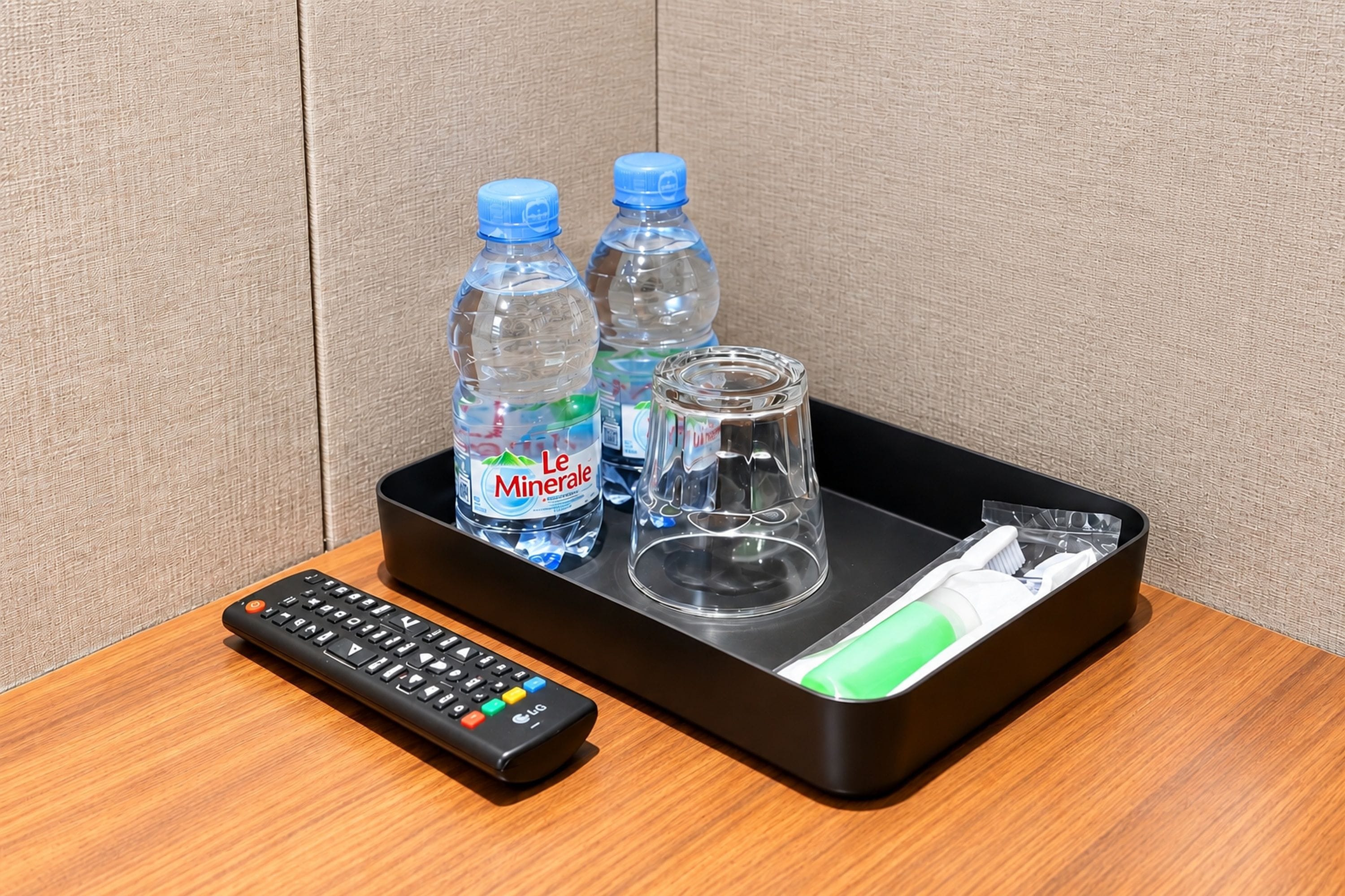 A tray with two water bottles, a glass, a remote control, and a toothbrush on a wooden surface.