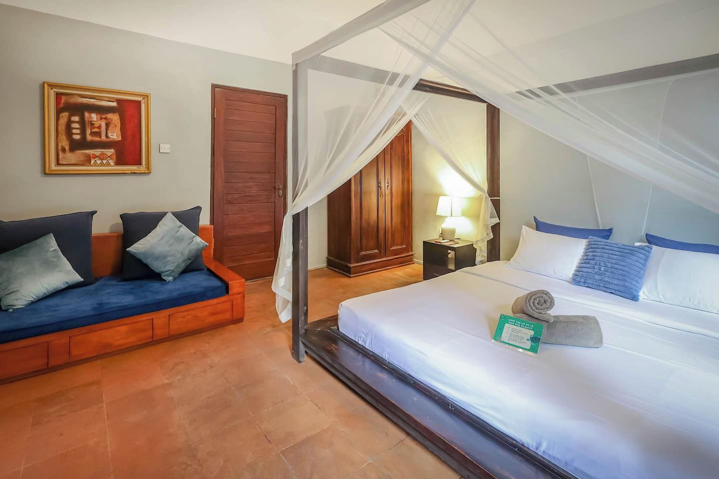 A hotel room with a bed, a sofa, a nightstand, and a door.