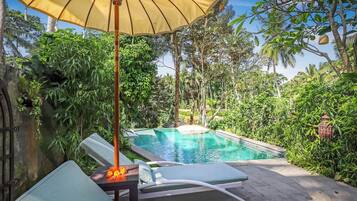 A pool area with lounge chairs and a table, surrounded by lush greenery.
