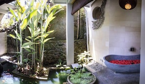 Un giardino interno tranquillo con stagno per carpe koi, piante in vaso e una parete in pietra.