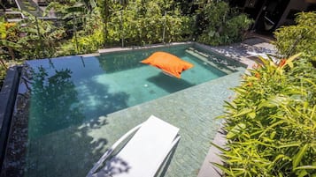 A clear swimming pool with a single orange cushion, surrounded by lush greenery.
