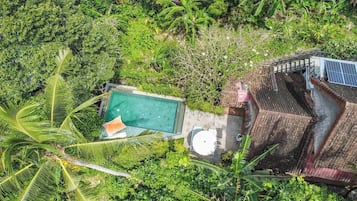 An aerial view of a property with a swimming pool surrounded by lush greenery, a covered patio area, and a solar water heater.