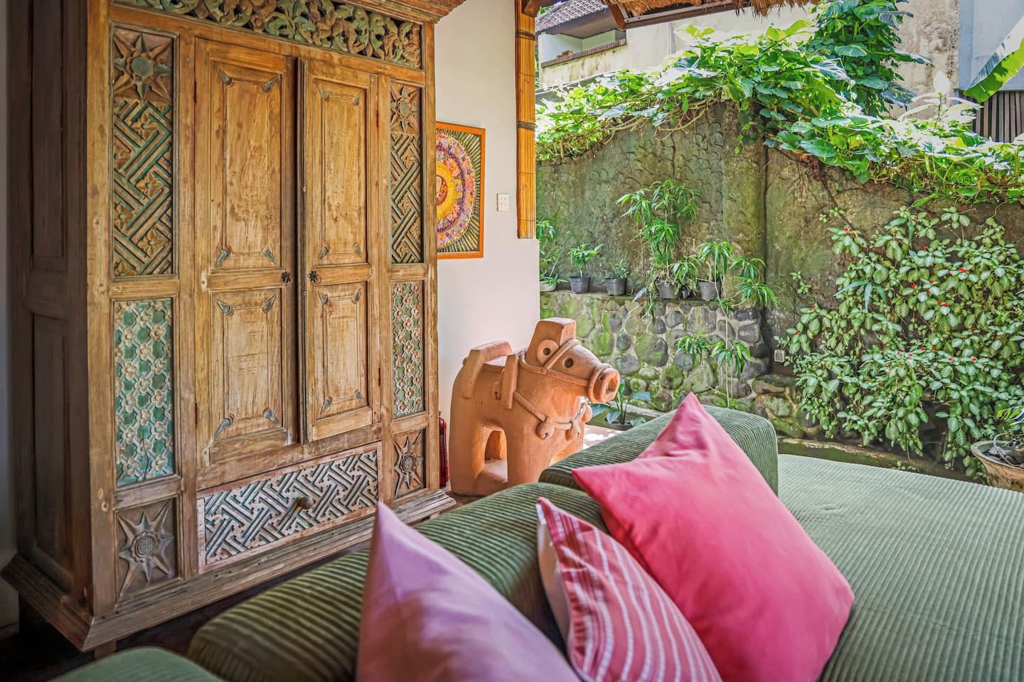 A room with a wooden cabinet, a decorative horse sculpture, and a view of a garden with plants and a stone wall.