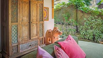 A room with a wooden cabinet, a decorative horse sculpture, and a view of a garden with plants and a stone wall.