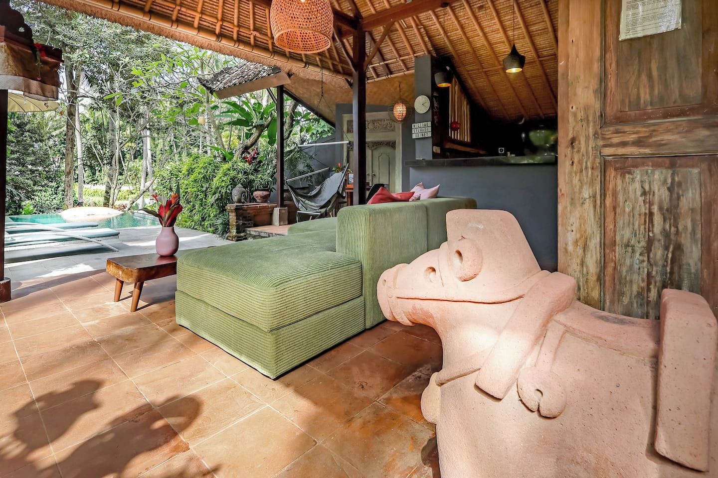 A covered outdoor seating area with a pool, a green sofa, and a stone sculpture.