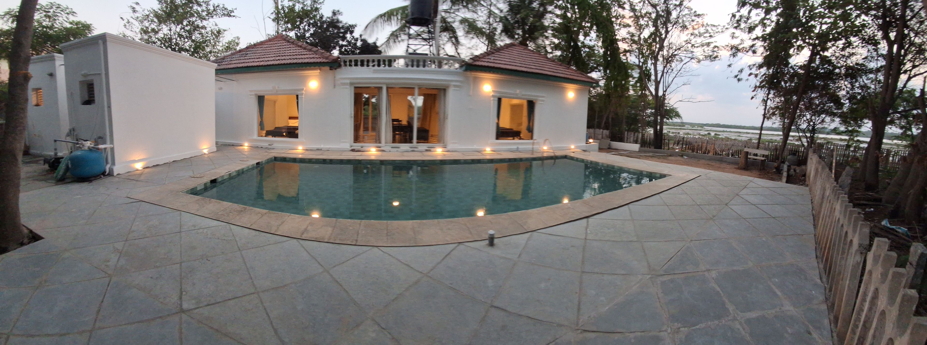 A swimming pool with a tiled deck, a small building with windows, and a view of the water.