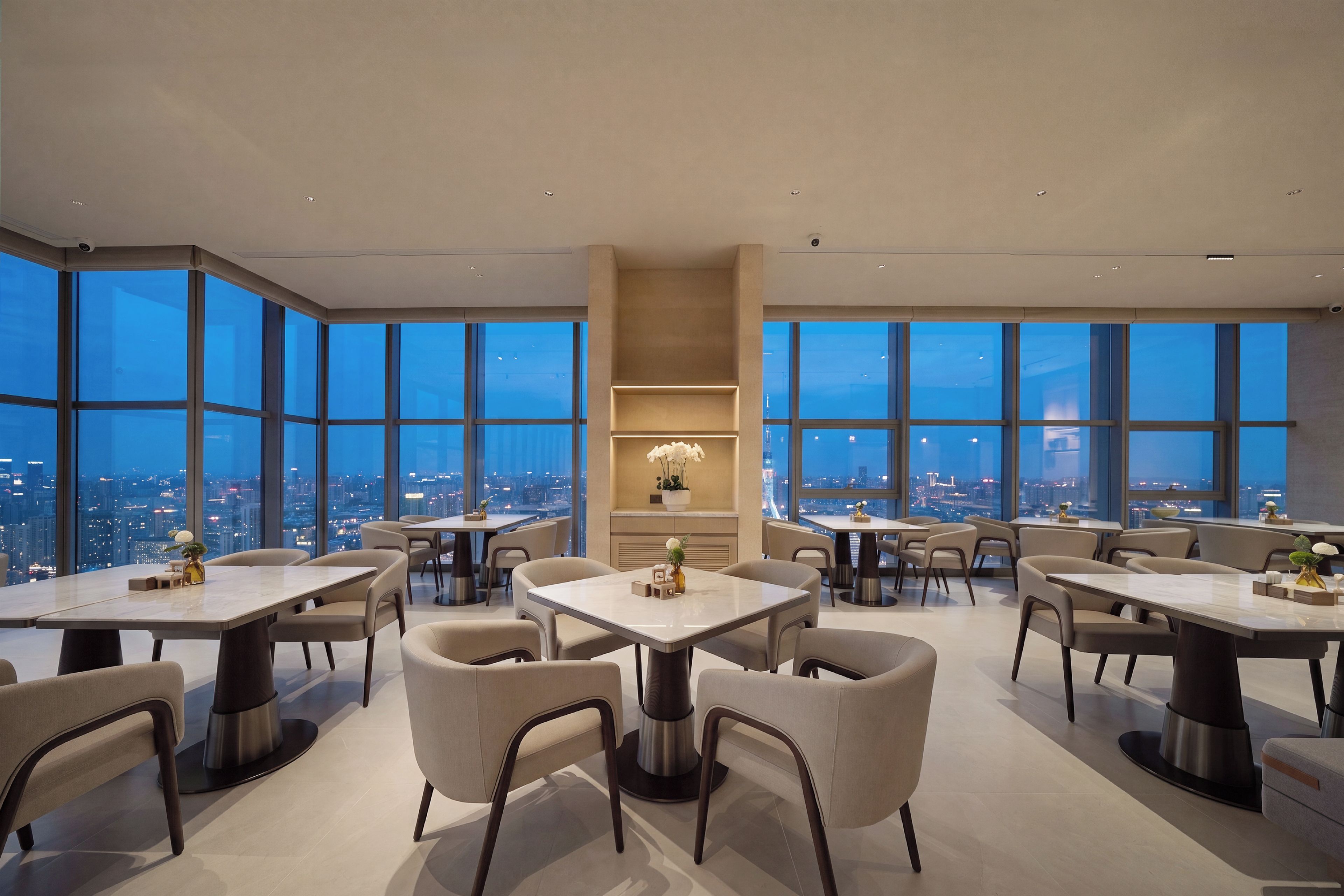 Un comedor moderno con varias mesas y sillas, ventanas amplias que ofrecen vista a la ciudad y una estantería central con objetos decorativos.