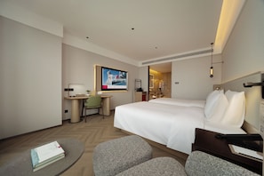 Habitación de hotel con una cama grande, un escritorio con silla, una mesita redonda y un televisor.