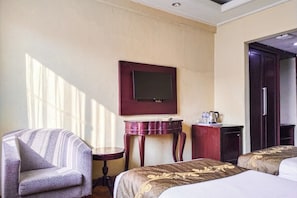 A hotel room with a bed, a chair, a small table, a television mounted on the wall, and a door leading to another room. - SNUZ Hotel Menteng (Jakarta)