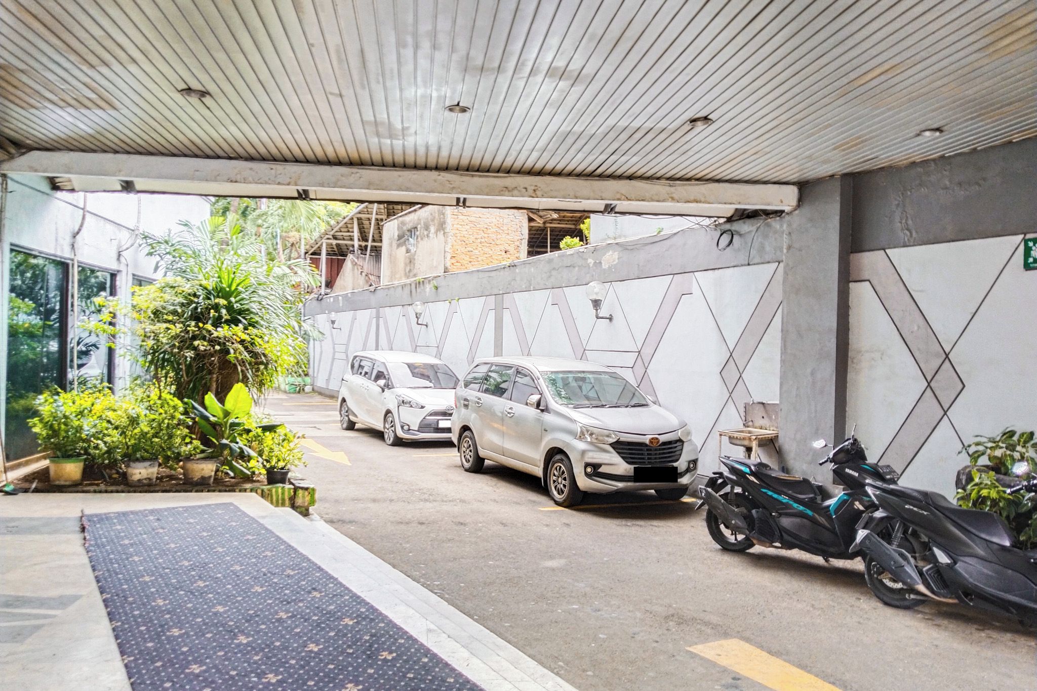 Un espace de stationnement couvert où sont garées deux voitures et une moto.