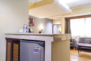 A hotel room with a kitchenette, a refrigerator, a water dispenser, and a sofa. - SNUZ Hotel Menteng (Jakarta)