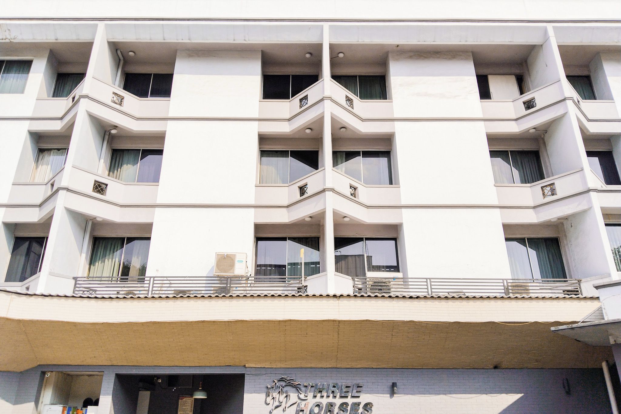 Un immeuble à plusieurs étages, doté d’une façade sobre, de balcons et d’une enseigne indiquant « TROIS CHEVAUX ».