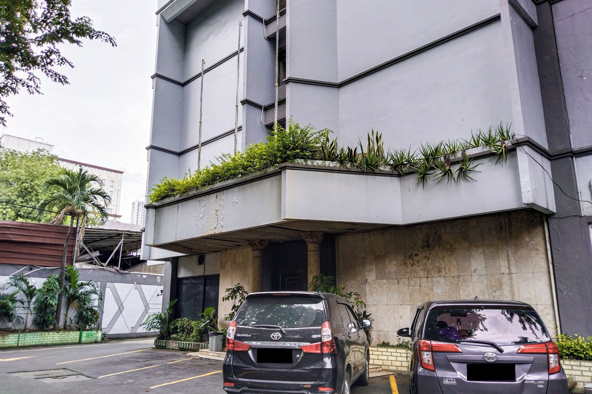 A parking area with two cars parked in front of a building with a flat roof and a concrete facade.