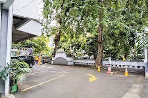 A parking area with a car, a tree, and a building in the background. - SNUZ Hotel Menteng (Jakarta)