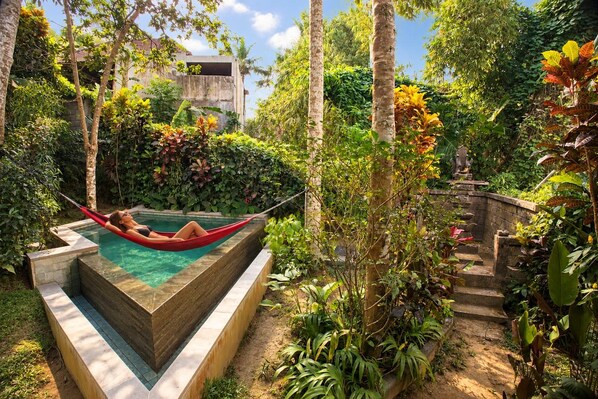 A pool area with a hammock, surrounded by lush greenery and a stone staircase.