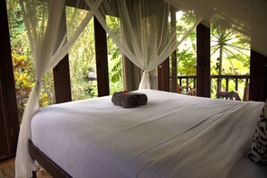 A bed with white linens, a rolled towel, and a canopy.