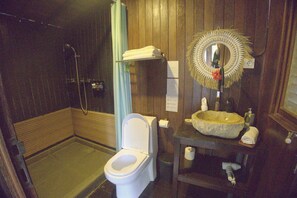 A bathroom with a toilet, a sink with a stone basin, a mirror with a decorative frame, and a shower area.