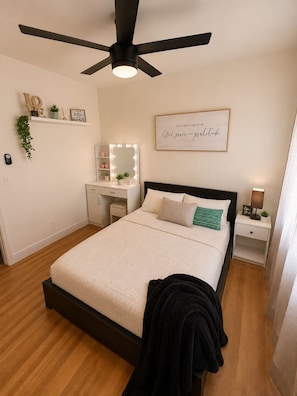 Une chambre à coucher avec un lit, une coiffeuse avec des lumières, un ventilateur de plafond et une citation inspirante sur le mur.