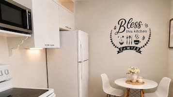 Eine moderne Küche mit weißen Geräten, einem Esstisch mit Stühlen und einer Wandsticker mit der Aufschrift 'Bless this kitchen FAMILY'.
