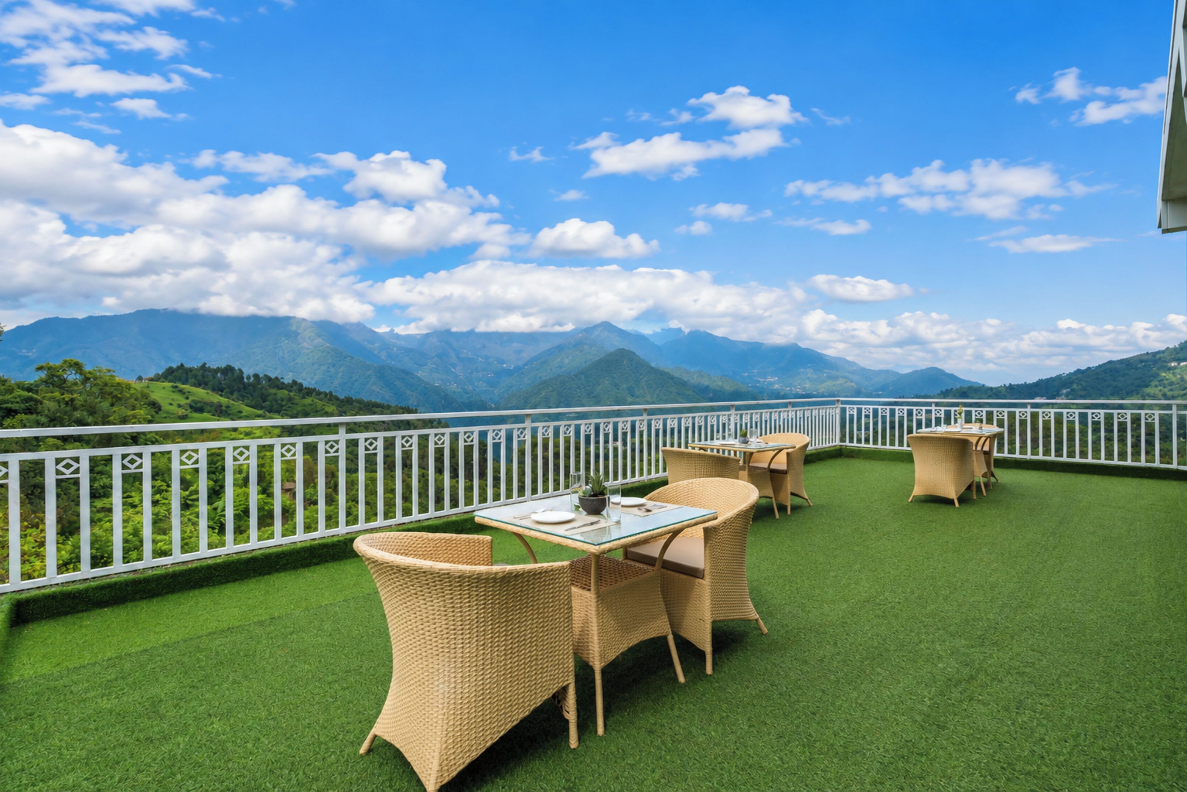 A terrace with wicker furniture and a glass table, overlooking a mountainous landscape.