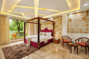 A four-poster bed with a red headboard, a marble floor, a view of greenery outside, and a Buddha mural on the wall.