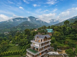 A multi-story building with a balcony, surrounded by lush greenery and mountains in the background. - ELIVAAS Signature SECRET ESCAPE Maharaj (Solan)