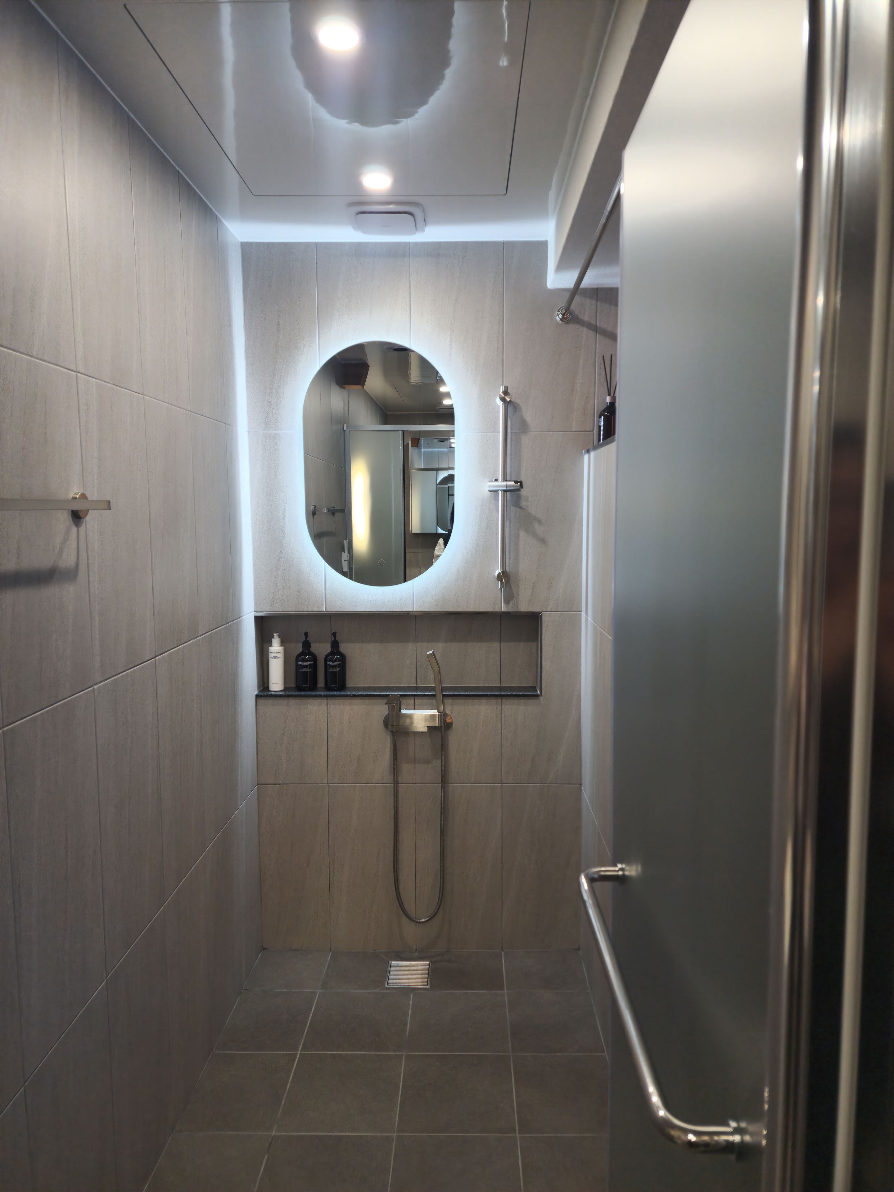 A modern bathroom with a walk-in shower, a mirror, and a shelf with toiletries.