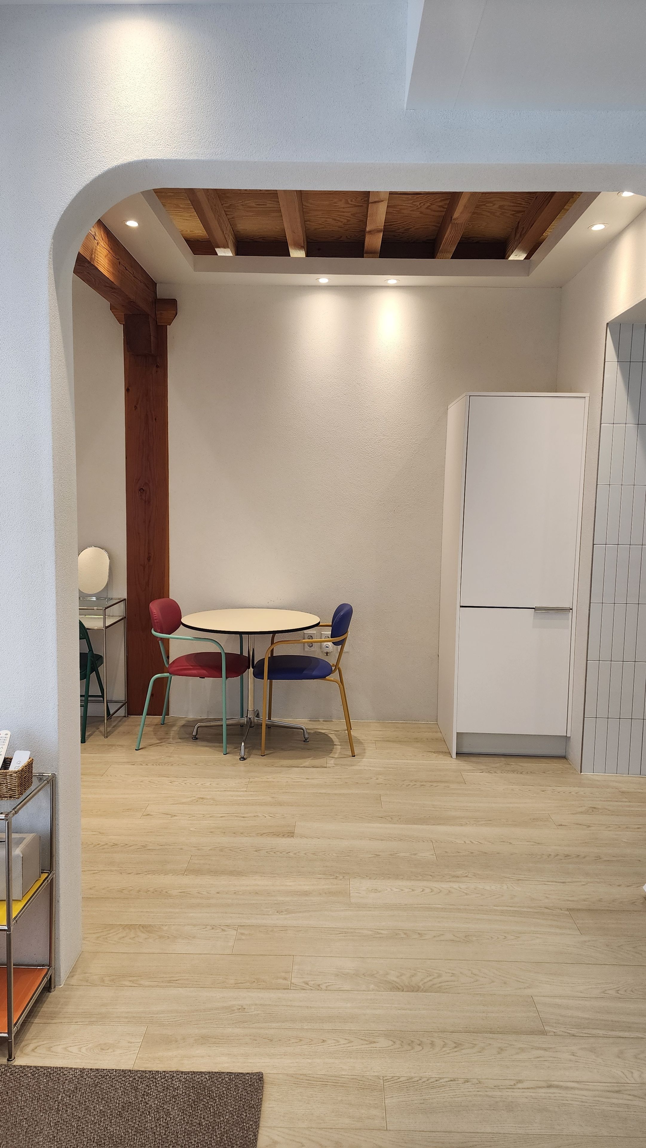 A room with a wooden ceiling, a white wall, a white cabinet, and a round table with chairs.