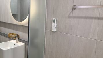 A bathroom with a glass shower enclosure, a white sink, a round mirror, and a towel rack.
