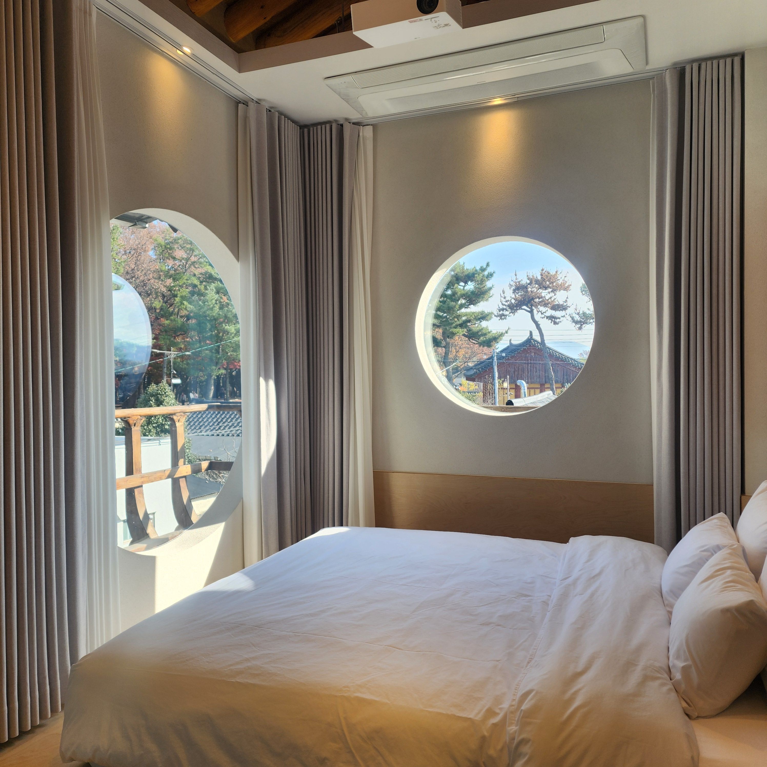 A hotel room with a bed, a circular window, and curtains.