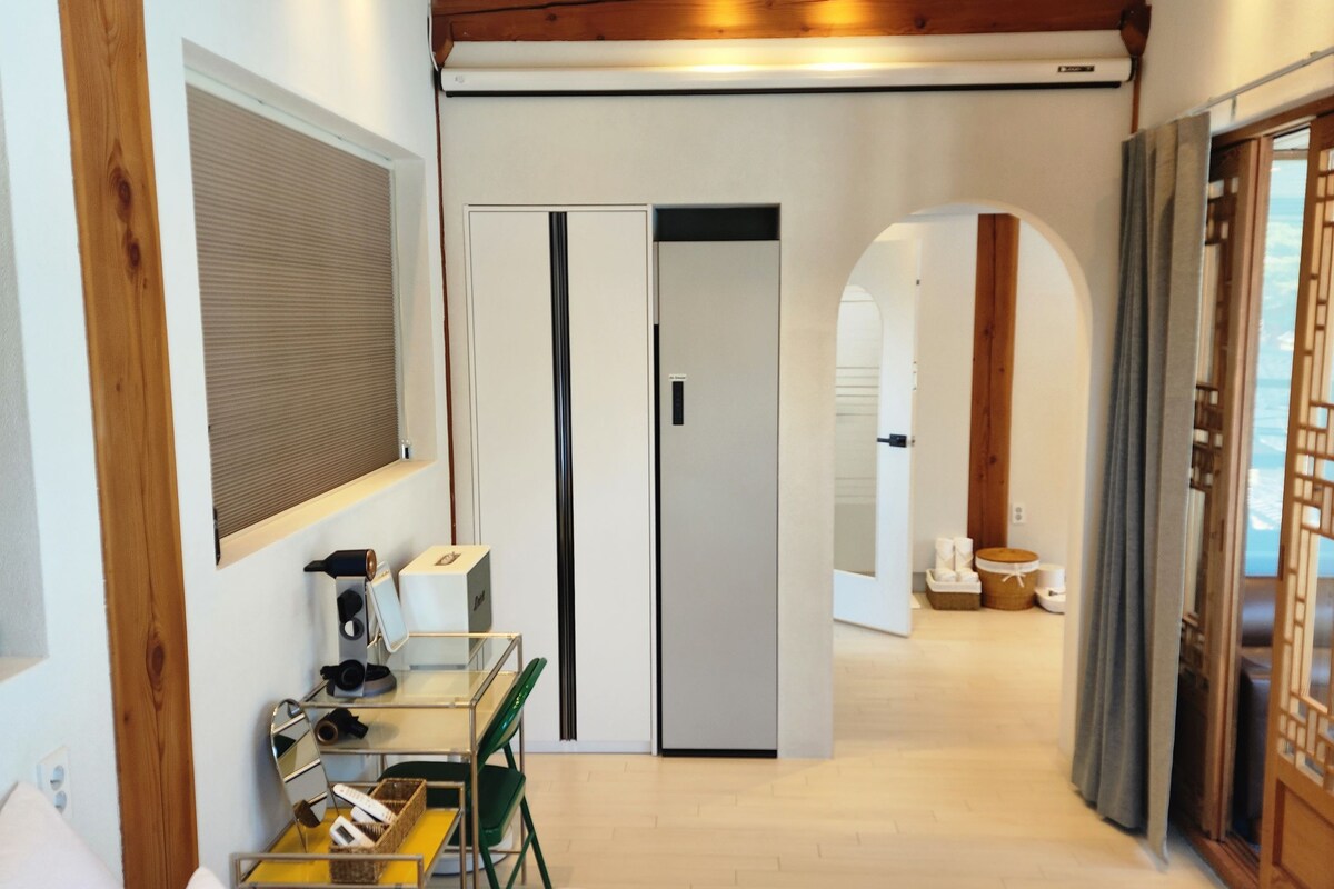 Habitación de hotel con cama, escritorio con silla, espejo y armario. Se observa una puerta que da a otra habitación.