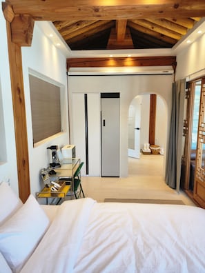 Ein Hotelzimmer mit einem Bett, einem Schreibtisch mit Stuhl, einem Spiegel und einem Kleiderschrank. Eine Tür führt in einen weiteren Raum.