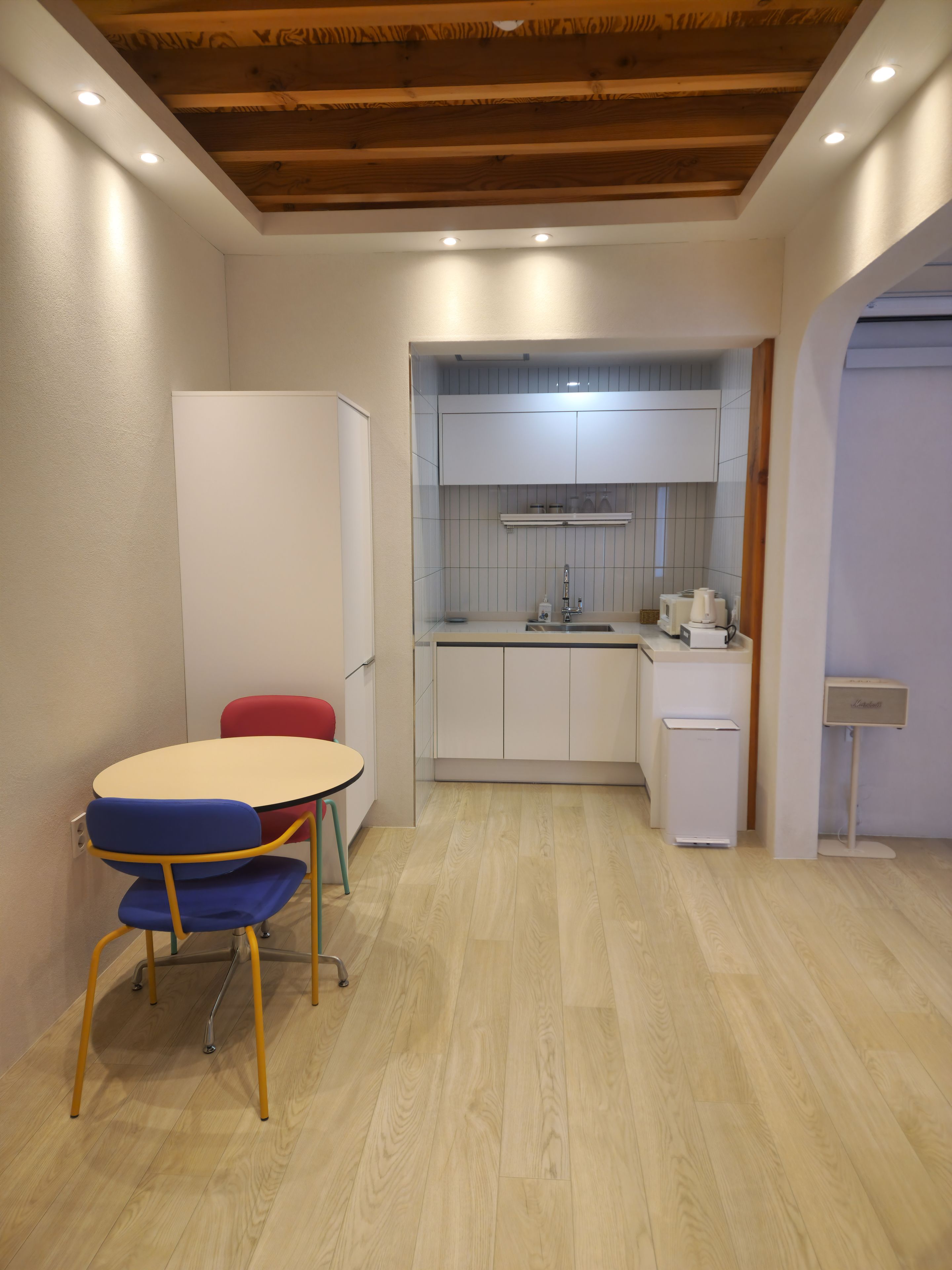 Une cuisine compacte avec des meubles blancs, un petit évier et un plan de travail sur lequel se trouve une bouilloire.