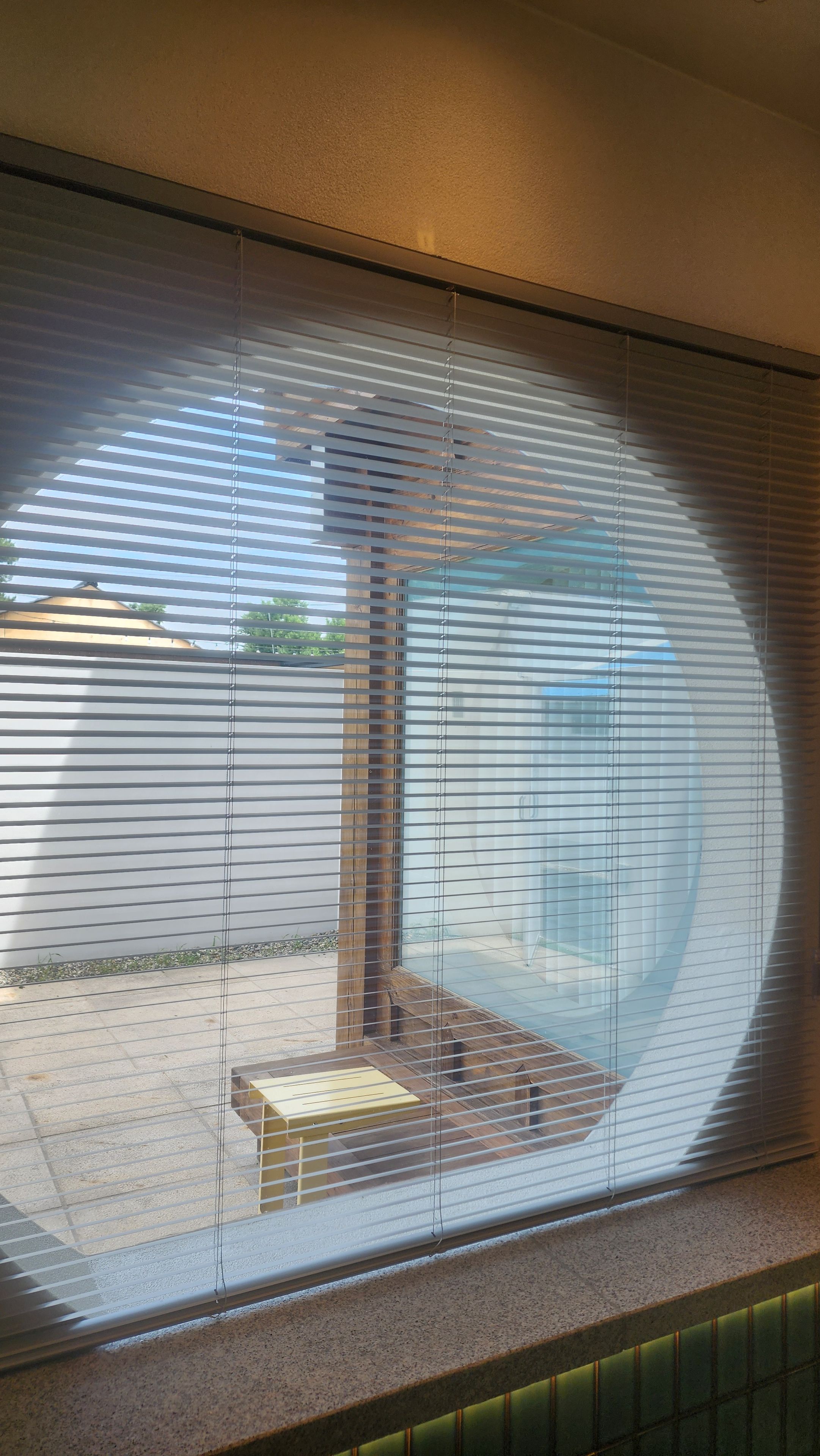 A room with a large window covered by blinds, a small table, and a bench.