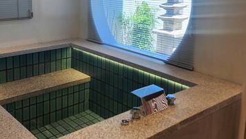 A spa room with a stone bathtub, a small table with a towel, and a window with blinds.