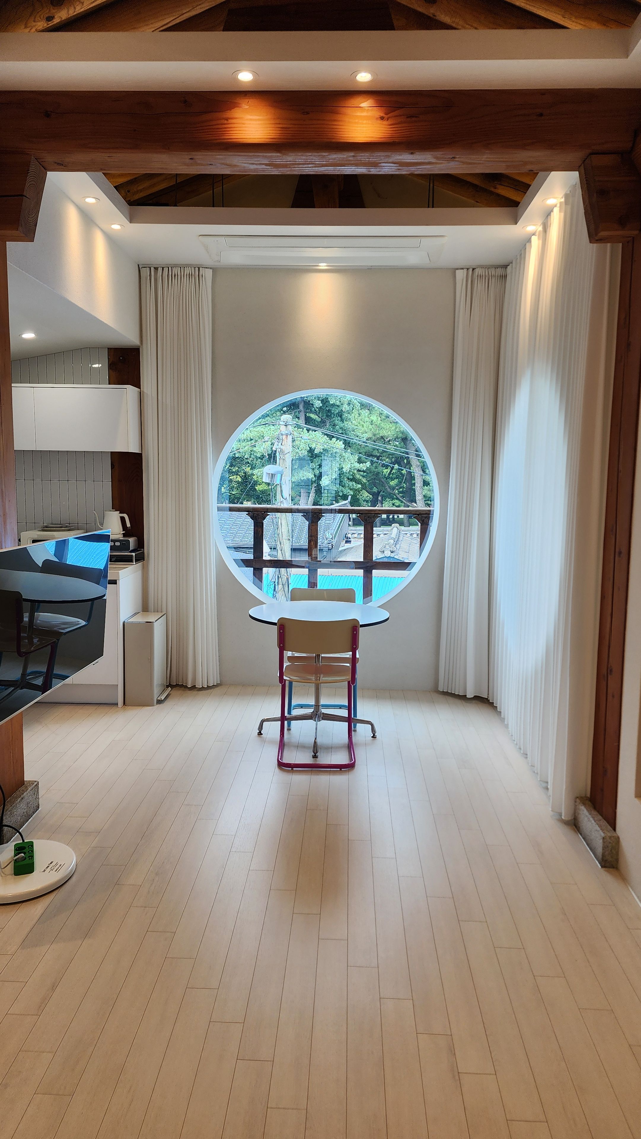 Een kamer met een eettafel, stoelen, een uitzicht door een rond raam en een keuken met inbouwapparatuur.