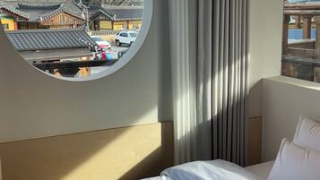 A hotel room with a bed, a round window with a view of traditional buildings, and a curtain.