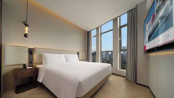 Habitación de hotel con una cama grande, una mesita de noche con un teléfono, un televisor de pared y una ventana con vista a la ciudad.