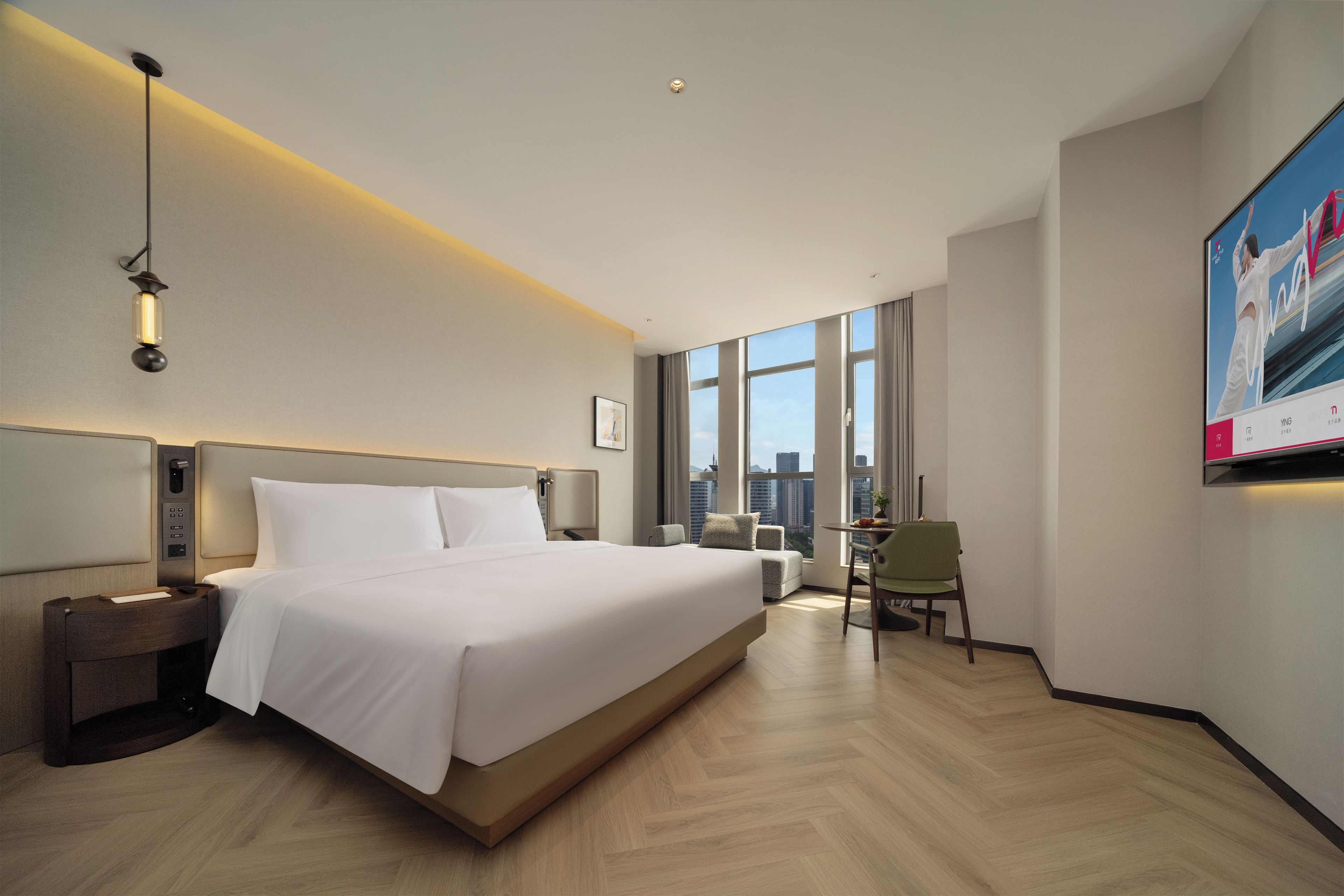 A hotel room with a large bed, a desk, a chair, and a TV on the wall.