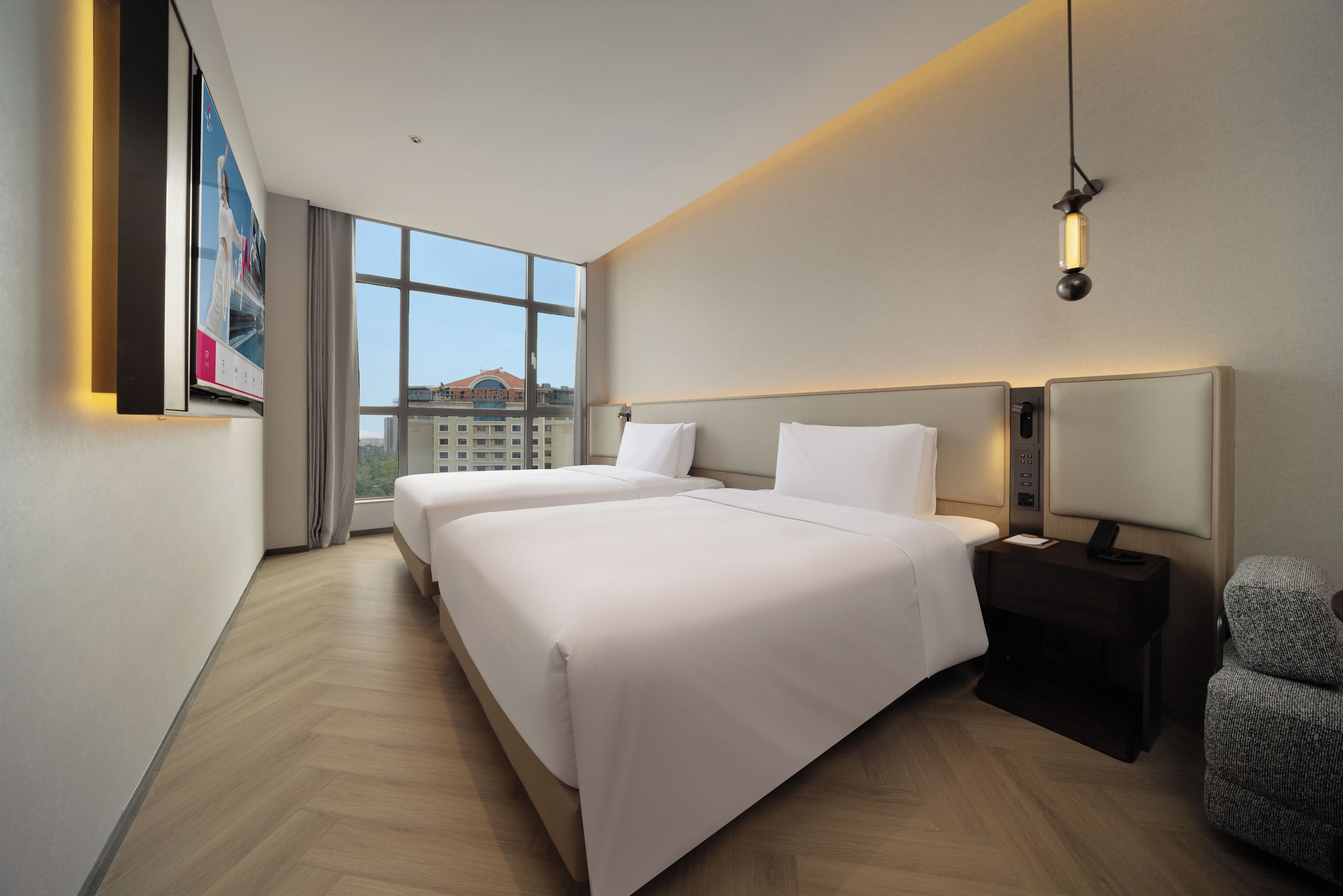 A hotel room with two beds, a large window, a desk with a lamp, and a chair.