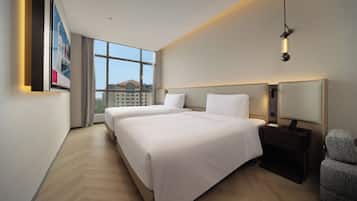 A hotel room with two beds, a large window, a desk with a lamp, and a chair.