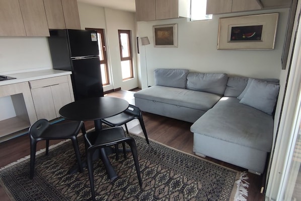 Un espacio habitable compacto con kitchenette, un sofá, una mesa de comedor con sillas y una alfombra estampada.