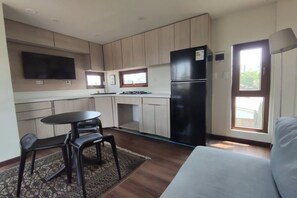 Una cocina compacta con comedor, un refrigerador negro y un televisor montado en la pared.