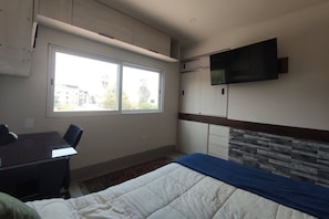 Un dormitorio con una cama, un escritorio, una silla, un televisor y una ventana.