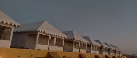 A row of white tents with windows, arranged in a line on a sandy ground.