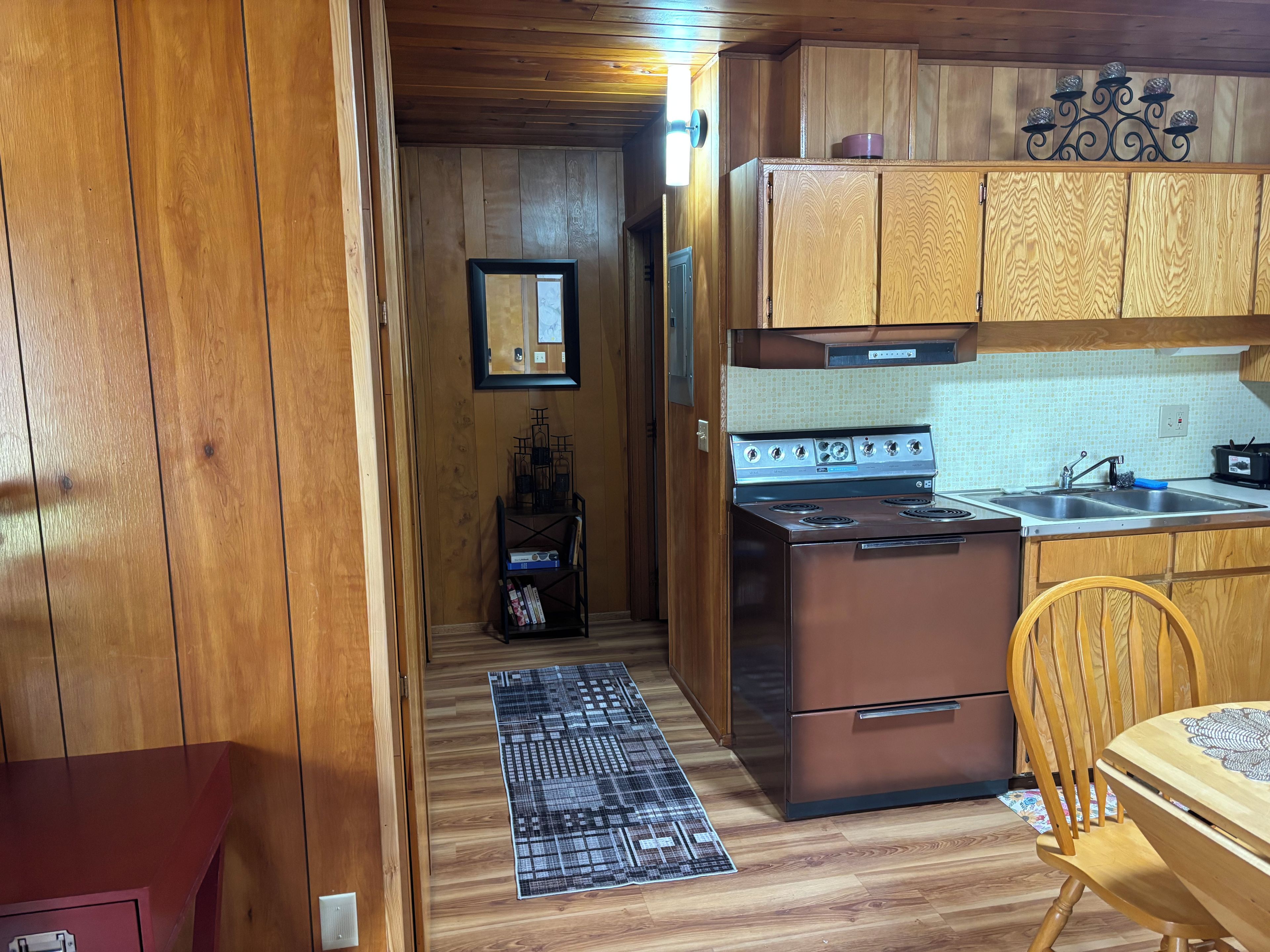 A wooden-paneled kitchen with a stove, sink, and wooden cabinets.