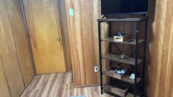 A room with a wooden door, a television on a metal stand, and a wooden floor.